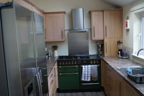 A kitchen with a stainless steel refrigerator, a gas stove, and wooden cabinets. - 3-Bed Pet-Friendly Cottage & Garden (Kirriemuir)