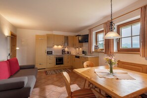 A compact kitchen with wooden cabinets, a dining table, and a view of the outdoors through a window. - Salvenalm Guesthouse - Apartments in the Heart of the Skiwelt Wilder Kaiser/Brixental (Salvenberg)
