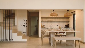 A modern kitchen with a dining area, featuring a staircase, a dining table set for four, and a hanging light fixture. - Rua Sapanca (Sapanca)