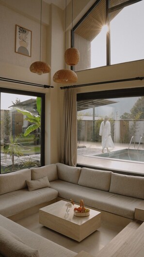 A modern living room with a beige sofa, a coffee table with fruit, and large windows overlooking a garden. - Rua Sapanca (Sapanca)