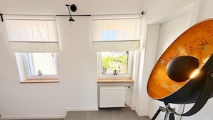 A room with two windows, a radiator, and a large brass speaker on a stand.