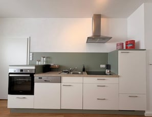 A compact kitchen with a built-in oven, dishwasher, and a stainless steel range hood.