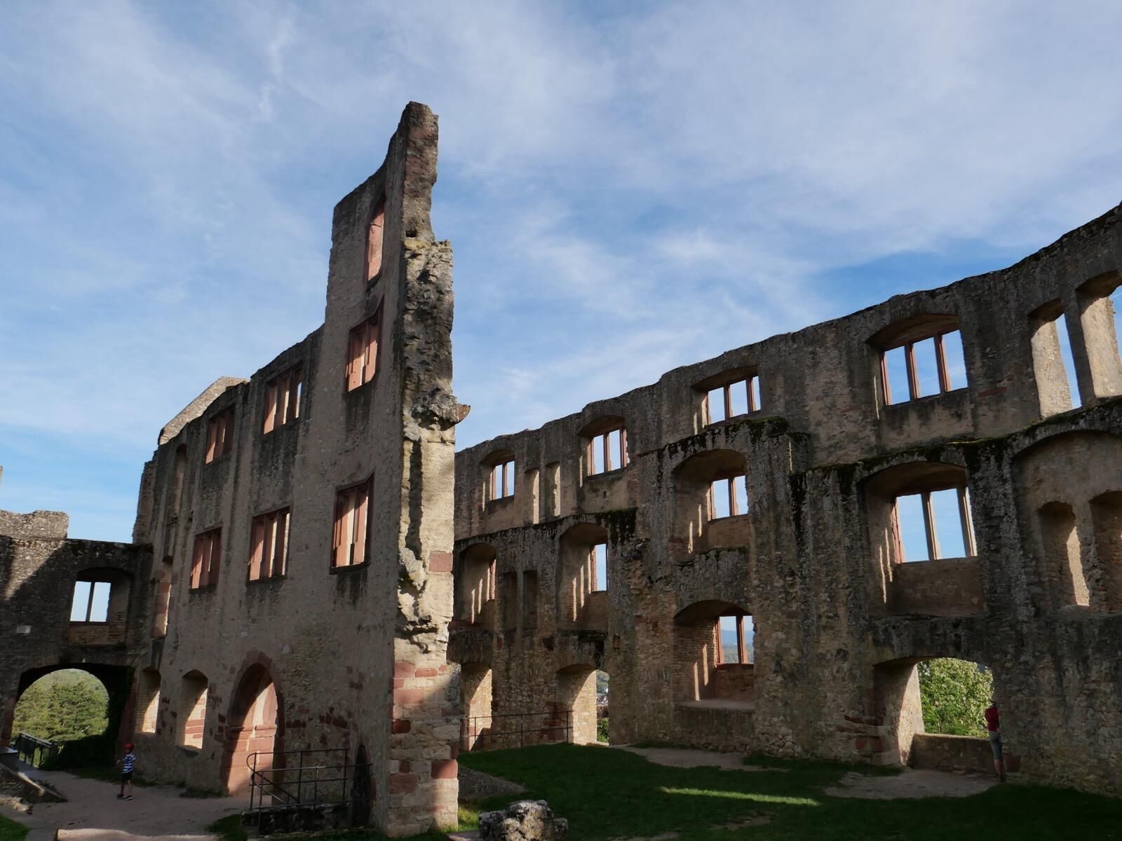 An ancient stone building with multiple arches and windows, surrounded by a grassy area.