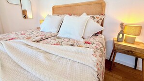 A bed with a floral bedspread, white pillows, and a woven headboard. There are two bedside lamps on wooden nightstands.