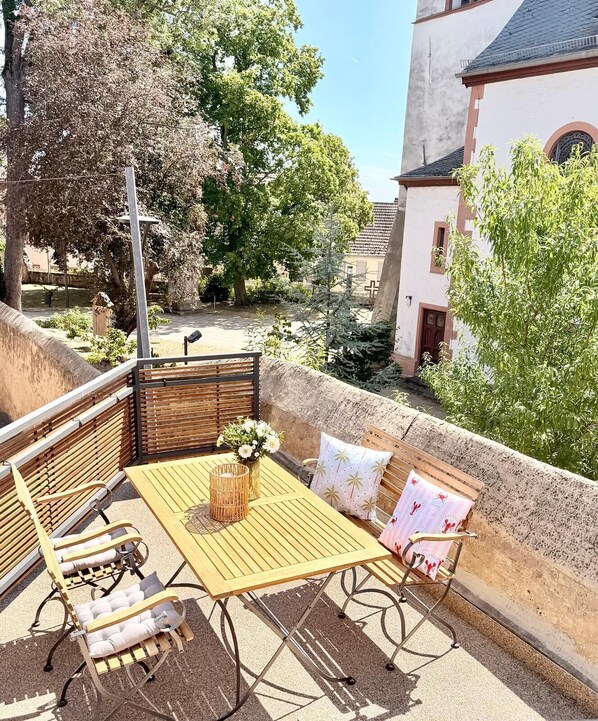 A patio with a wooden table and chairs, a cushioned bench, and a small potted plant.