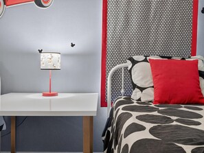 A bedroom with a white bedside table, a red lamp, a patterned wall, and a bed with a black and white patterned bedspread and a red pillow. - 8BR Pool/Spa, Themed Movie,Games and Kids Rooms. Disney area Waterpark Resort (Davenport)