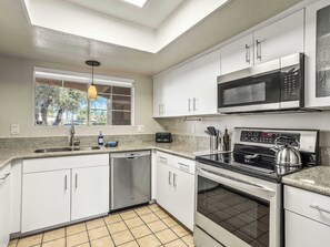 A modern kitchen with white cabinets, a stainless steel microwave, a gas stove, and a dishwasher. - Mesquite Oasis Palm Springs (Palm Springs)