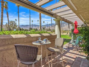 An outdoor patio with wicker chairs, a table with blue and white patterned cups, and a red umbrella. - Mesquite Oasis Palm Springs (Palm Springs)