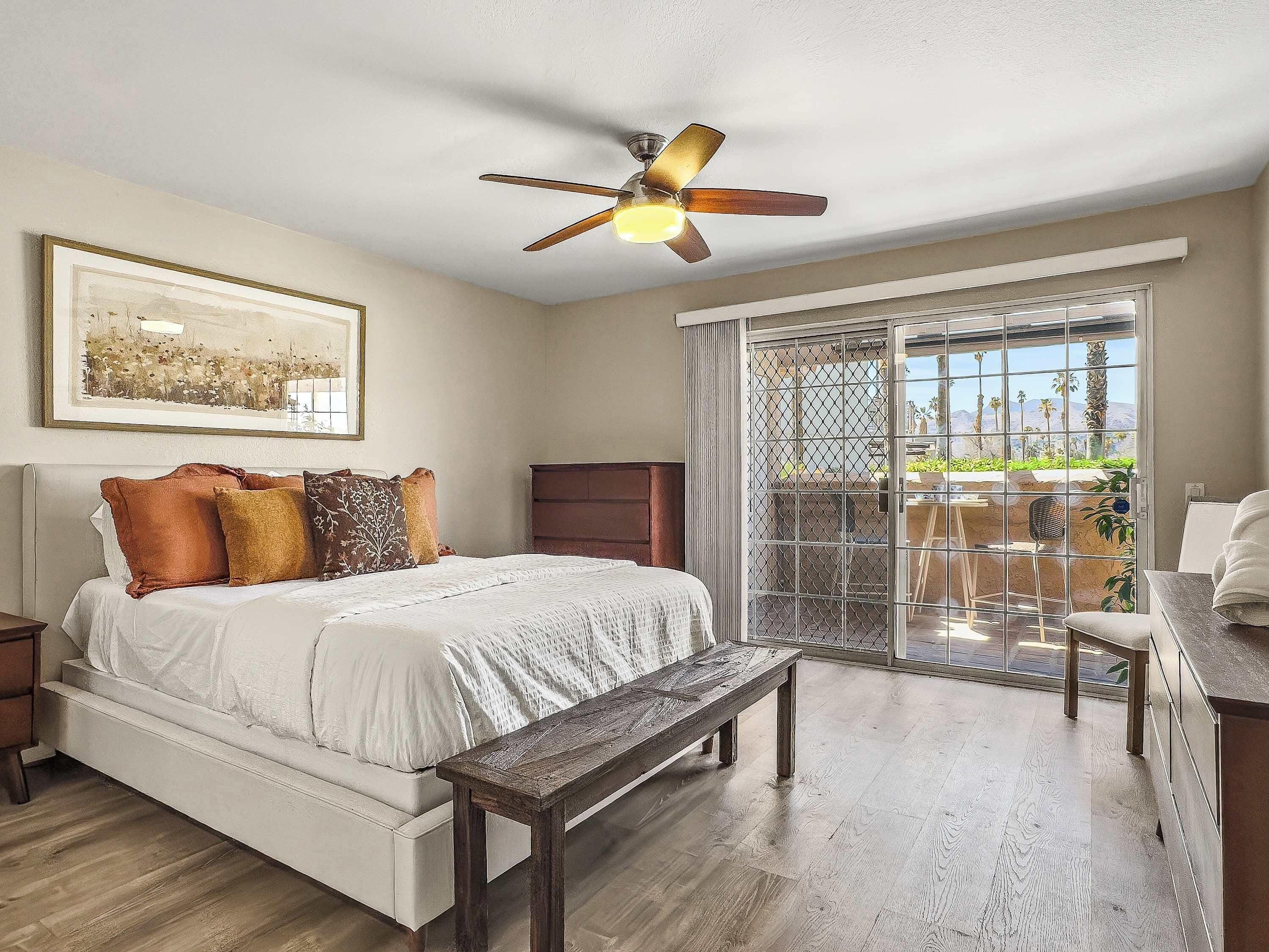 Une chambre à coucher comprenant un lit, un banc, un ventilateur de plafond, une fenêtre avec vue et une porte donnant sur un balcon.