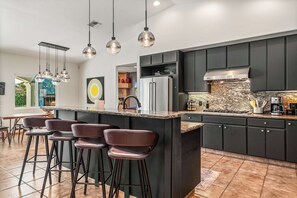 A modern kitchen with a central island, bar stools, and a dining area with a view. - Limonata Palm Springs (Palm Springs)
