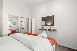 A hotel room with a bed, a mirror, a shelf with decorative items, and a door leading to a bathroom. - Limonata Palm Springs (Palm Springs)
