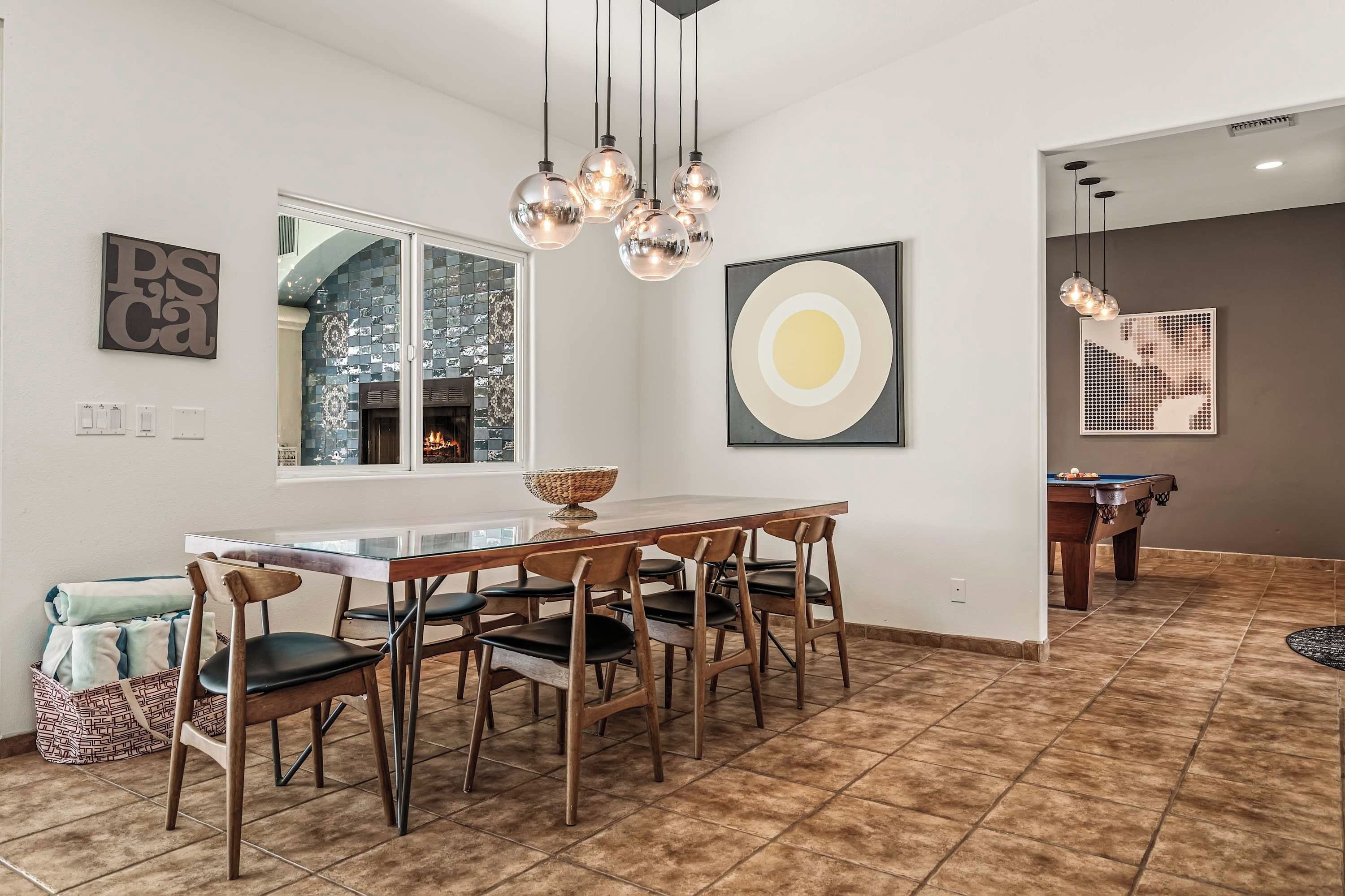 Uma área de refeições moderna com mesa de vidro, cadeiras de madeira e uma luminária central.