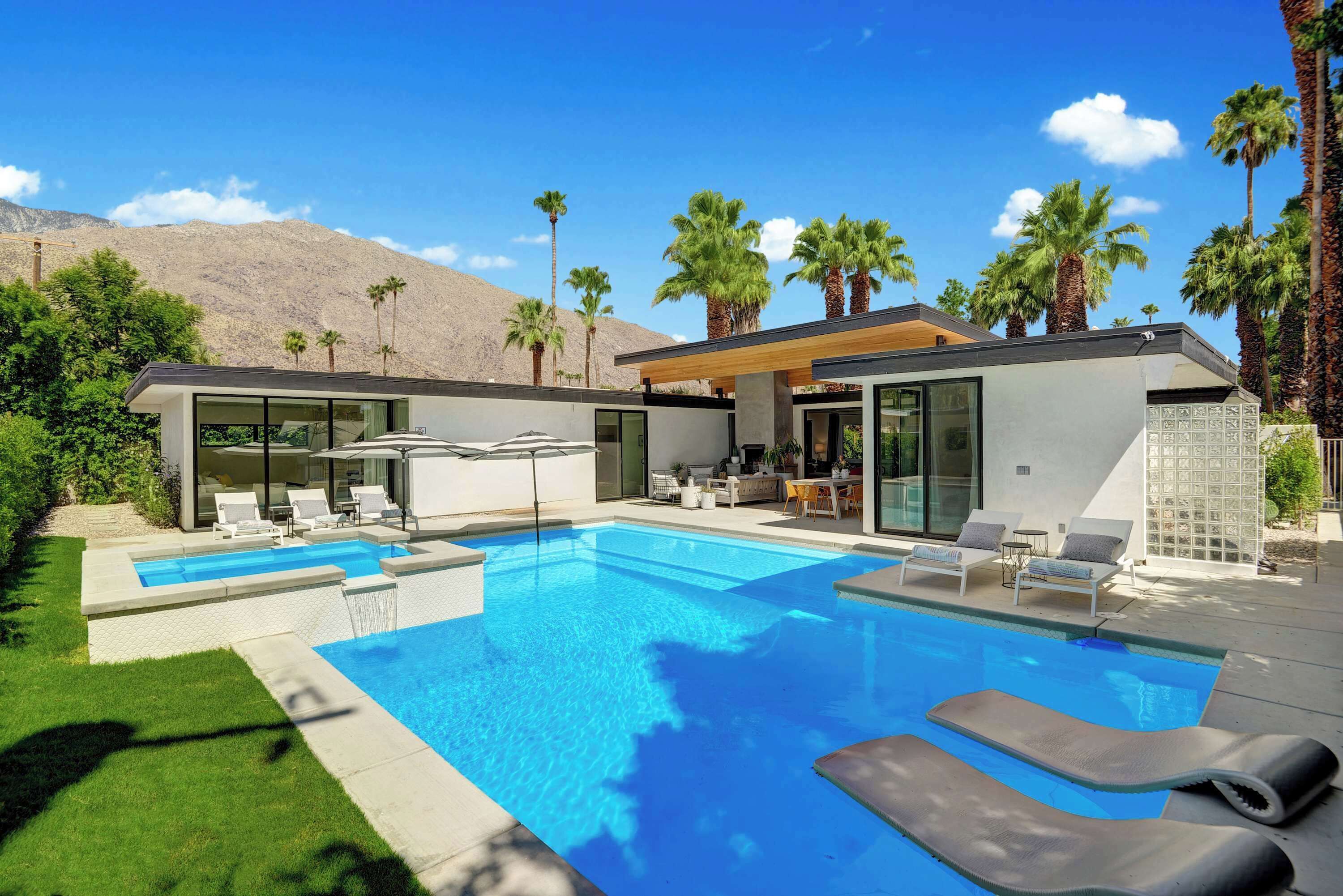 A modern house with a swimming pool, outdoor furniture, and palm trees.