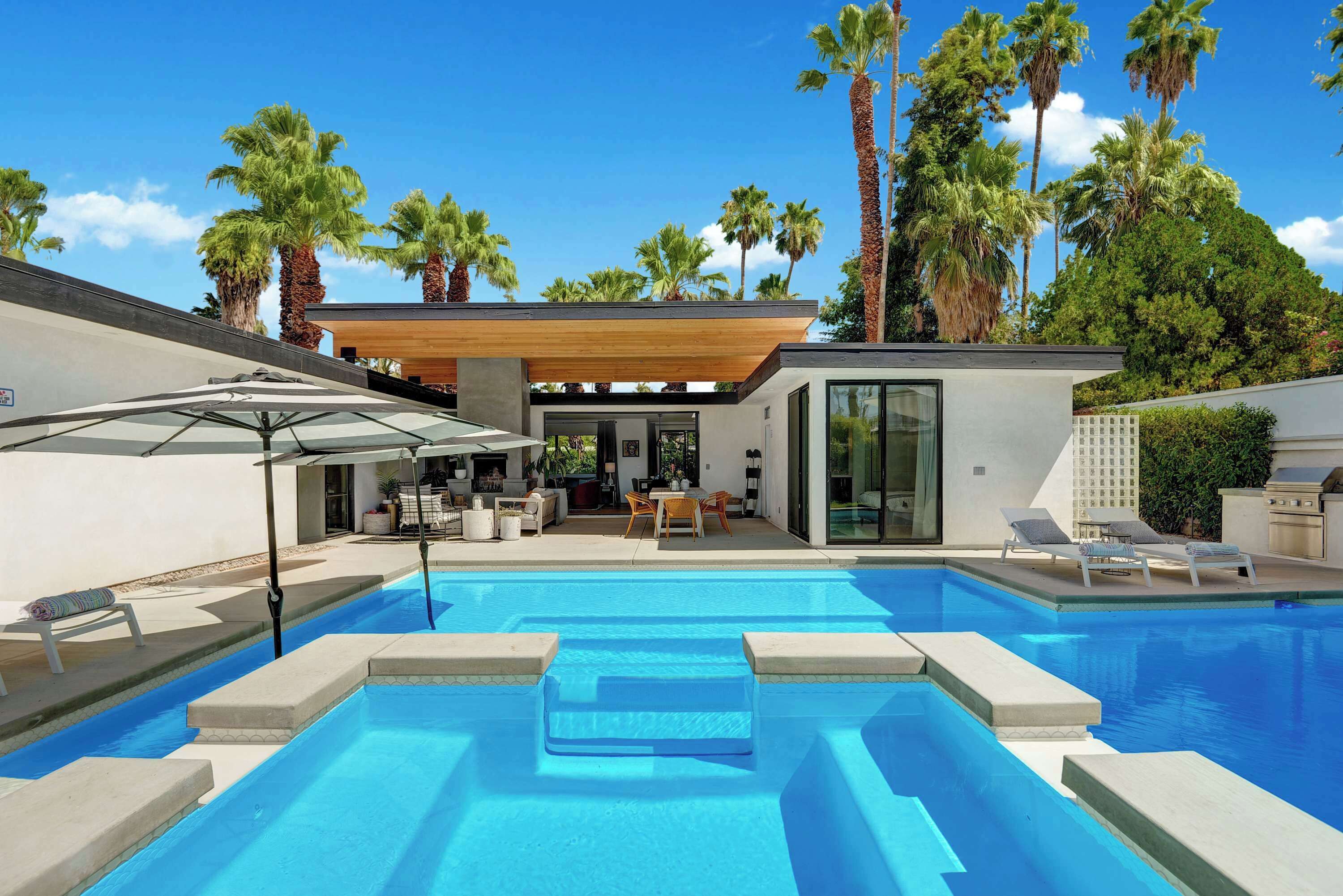A modern outdoor pool area with a covered seating area, lounge chairs, and a wooden pergola.