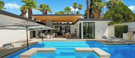 A modern outdoor pool area with a covered seating area, lounge chairs, and a wooden pergola.