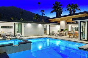 A modern outdoor pool area with a clear view of the mountains in the background, a covered seating area, and a well-lit patio. - Casa Palmera-Mid Century Modern (Palm Springs)