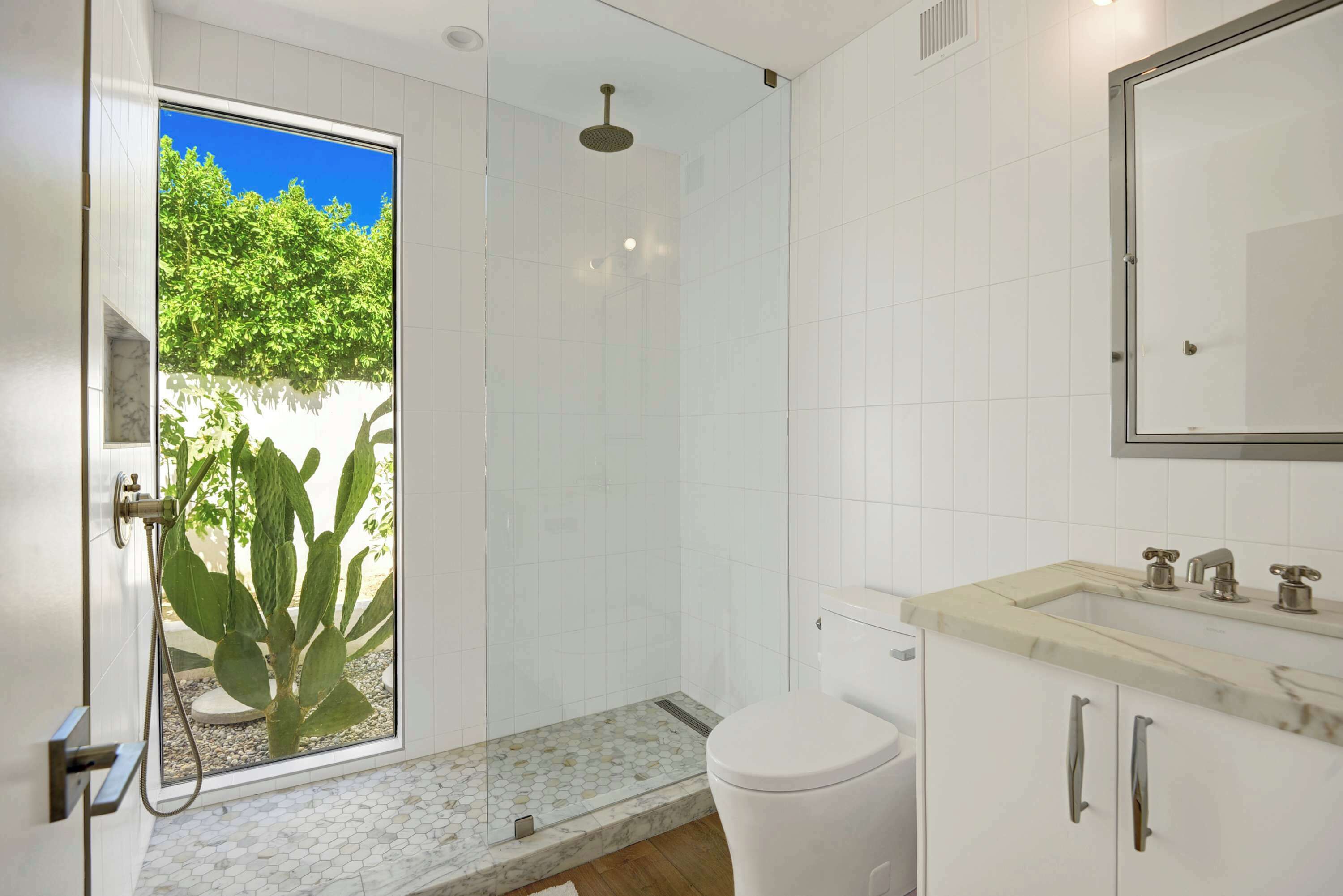 A modern bathroom with a glass shower enclosure, a toilet, and a sink with a marble countertop.