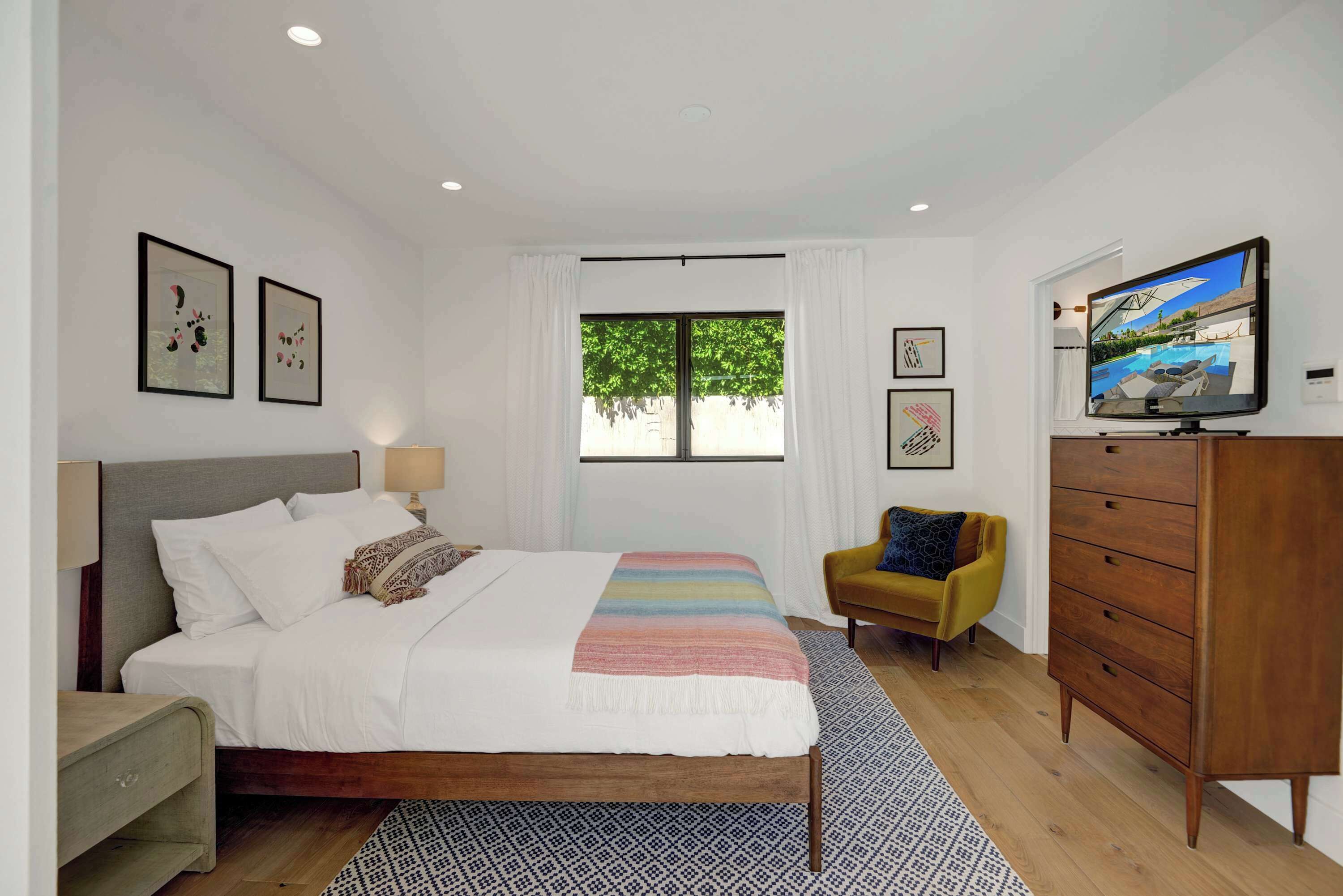 A bedroom with a bed, a TV, a wardrobe, and a window with a view of greenery.
