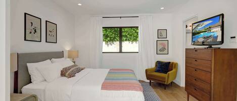 A bedroom with a bed, a TV, a wardrobe, and a window with a view of greenery.