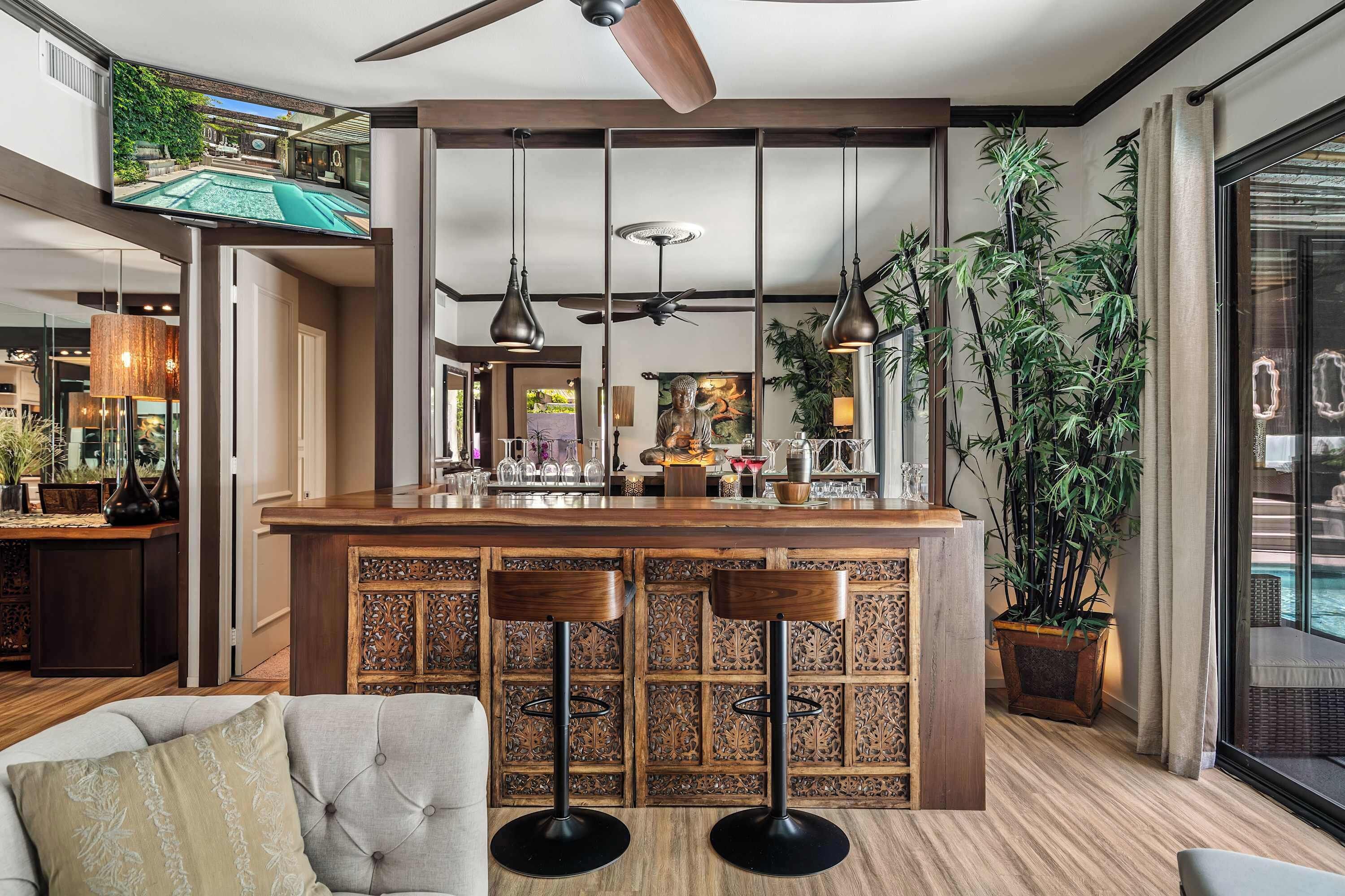 A modern bar area with a wooden counter, two bar stools, and a ceiling fan.