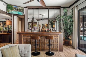A modern bar area with a wooden counter, two bar stools, and a ceiling fan. - Bali Sol with private pool and spa (Palm Springs)
