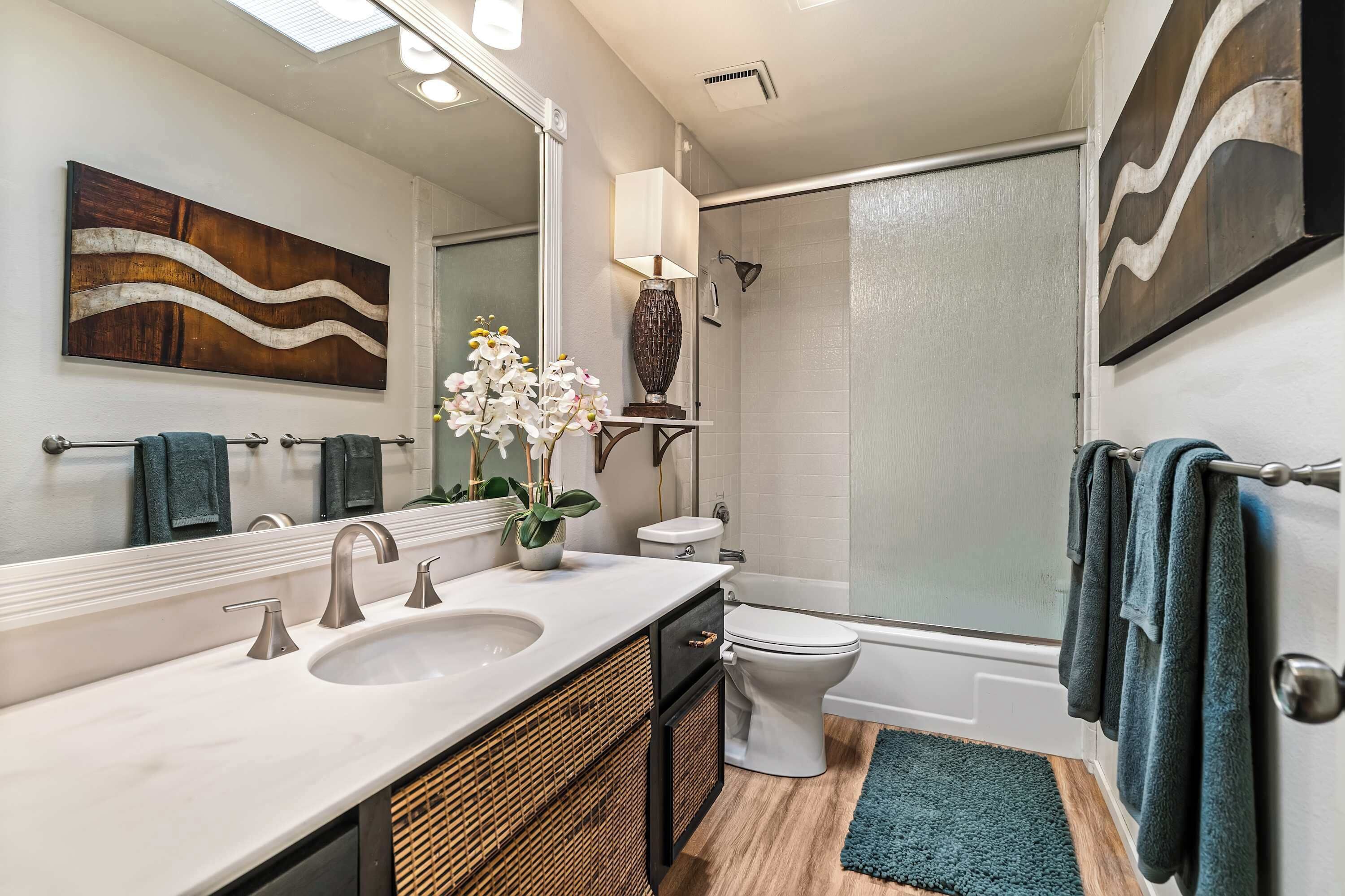 A modern bathroom with a large mirror, a sink with two faucets, a toilet, and a shower area.