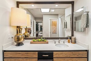 Une salle de bain avec un grand miroir, un lavabo, un porte-serviettes et une composition florale décorative.