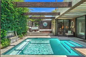 Une piscine avec un jacuzzi, un espace salon extérieur et une pergola.