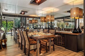 A modern dining area with a long wooden table, upholstered chairs, and pendant lighting. - Bali Sol with private pool and spa (Palm Springs)
