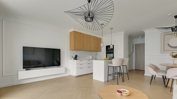 Ein modernes Wohnzimmer mit Flachbildfernseher, einem Essbereich mit rundem Tisch und einer Küche mit Holzausstattung.