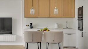 Eine moderne Küche mit Holzausstattung, Pendelleuchten, einer Kaffeemaschine, Obstschale und einem Fernseher.