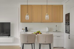 A modern kitchen with wooden cabinets, pendant lights, a coffee maker, fruit bowl, and a TV. - Przystań Letnica 40 | 3 Bedrooms | 2x Parking (Gdańsk)