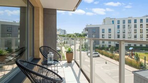Ein Balkon mit Sitzgelegenheit, einer Pflanze im Topf und Blick auf einen Parkplatz sowie Gebäude.