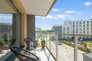 A balcony with a seating area, a potted plant, and a view of a parking lot and buildings. - Przystań Letnica 40 | 3 Bedrooms | 2x Parking (Gdańsk)