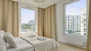 Ein Hotelzimmer mit einem Bett, zwei Fenstern und Blick auf Gebäude.