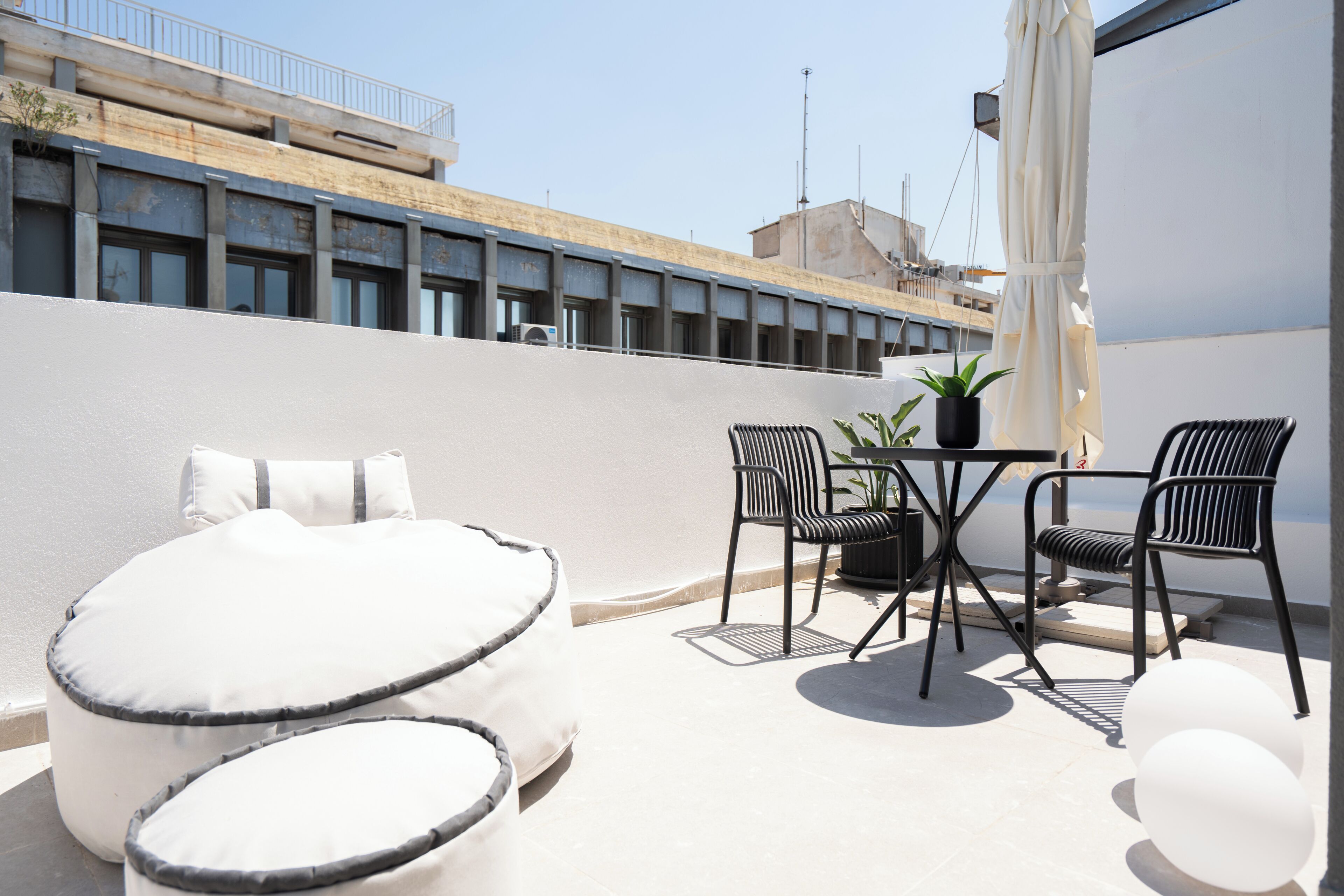 Une terrasse sur le toit avec un mur blanc, une petite table avec des chaises et un canapé blanc.