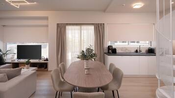 A modern living room with a round dining table, a flat-screen TV, and a kitchen area with a coffee maker.