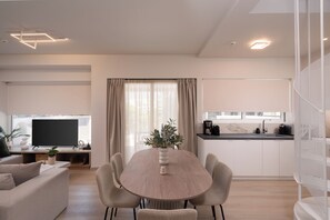 Una sala de estar moderna con una mesa de comedor redonda, un televisor de pantalla plana y una zona de cocina con cafetera.