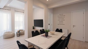 Una sala de estar moderna con un ventanal grande, un televisor de pantalla plana, una mesa de comedor con sillas y una pared con una frase motivacional.