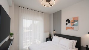 Un dormitorio moderno con una cama grande, un televisor de pantalla plana, una mesita de noche, una planta en maceta y una ventana con cortinas traslúcidas.