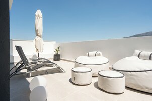 Una terraza en la azotea con una sombrilla blanca, sillones de descanso y otomanas.