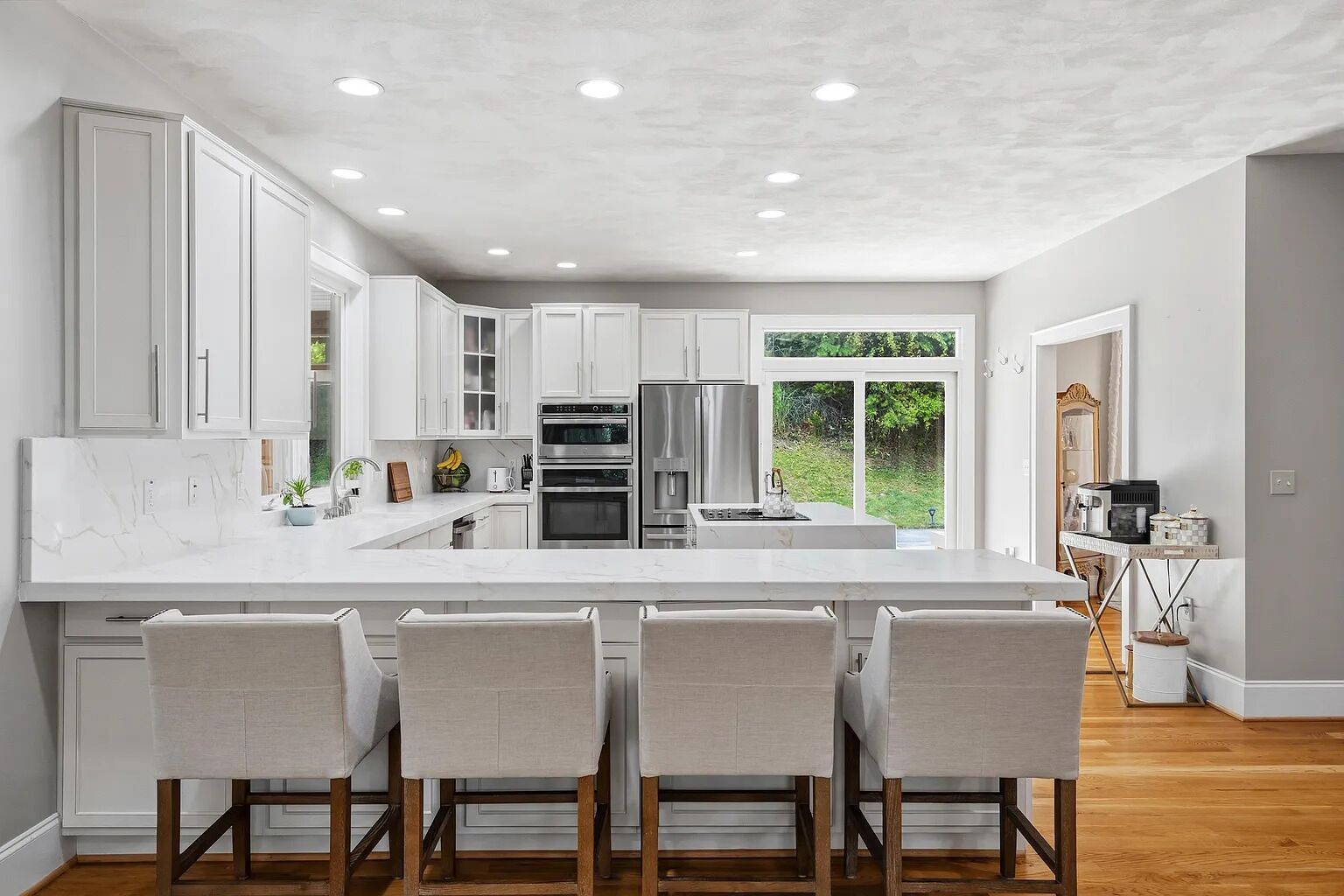 A modern kitchen with white cabinetry, a large island with bar stools, built-in appliances, and a view of the outdoors.