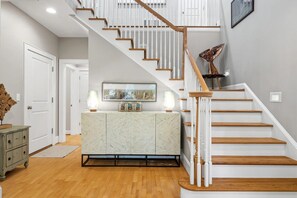 A staircase with wooden steps and white railings, leading to a landing with a marble cabinet and decorative items.
