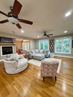 A spacious living room with a large sectional sofa, a patterned armchair, and a ceiling fan.