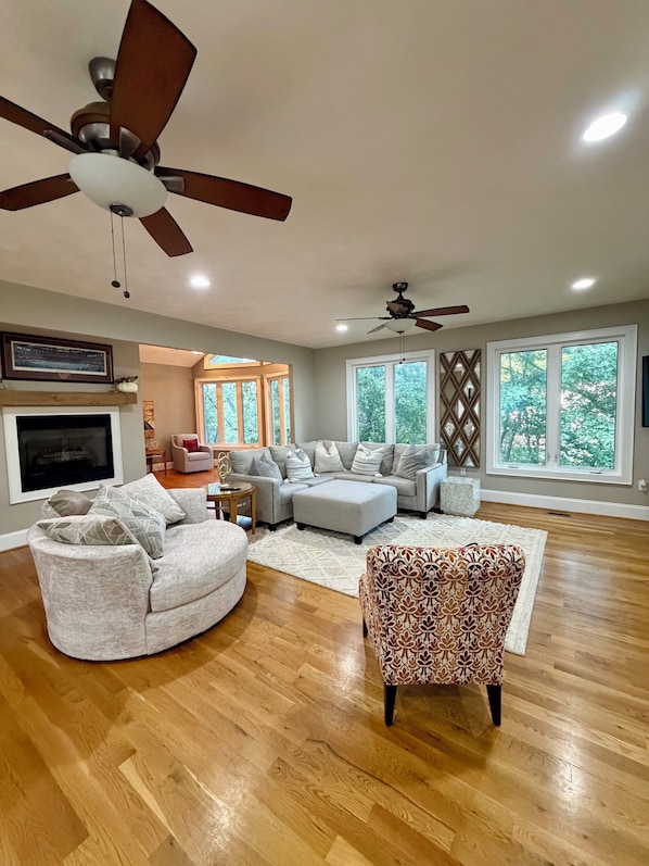 A spacious living room with a large sectional sofa, a patterned armchair, and a ceiling fan.