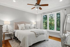A bedroom with a bed, bedside tables, a ceiling fan, and a window with curtains.