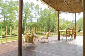 En overdækket terrasse med træborde og stole, omgivet af et træhegn og træer.