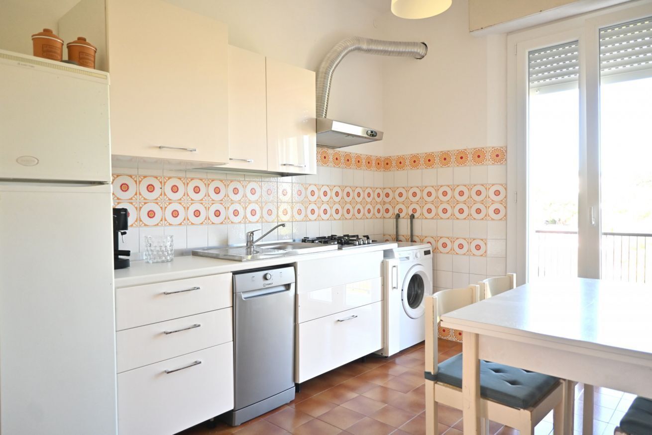 A kitchen with a dishwasher, washing machine, and a dining area with chairs.