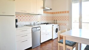 Cocina con lavavajillas, lavadora y comedor con sillas.