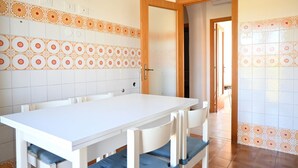Un comedor con una mesa y sillas blancas, un salpicadero de azulejos con diseños naranja y blanco, y una puerta de madera que da a otra habitación.
